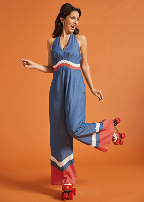 Woman wearing a retro blue jumpsuit with halter tie neckline and wide-leg silhouette.