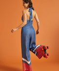 Back view of a woman wearing a halter jumpsuit with adjustable tie and smocked elastic back.