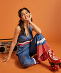 Woman seated in a blue halter jumpsuit featuring contrast stripe details and flowing legs.