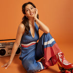 Woman seated in a blue halter jumpsuit featuring contrast stripe details and flowing legs.