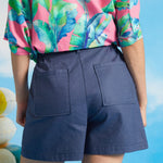 Back view of blue linen blend shorts with elastic waistband and patch pockets.