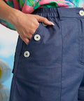 Close-up of decorative sailor button detail and front pocket on blue linen shorts.