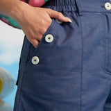 Close-up of decorative sailor button detail and front pocket on blue linen shorts.