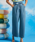 Woman wearing dusty blue cropped trousers with wide legs, pleated front, and removable waist tie