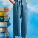 Woman wearing dusty blue cropped trousers with wide legs, pleated front, and removable waist tie