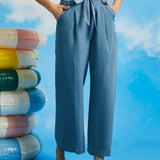 Woman wearing dusty blue cropped trousers with wide legs, pleated front, and removable waist tie