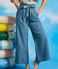 Woman wearing dusty blue high-waisted cropped wide leg pants with sash tie belt and pockets paired with a striped sleeveless top