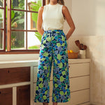 Woman wearing a white sleeveless top and blue patterned pants standing in a kitchen.