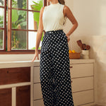 Woman in a white sleeveless top and black polka dot pants standing in a kitchen.