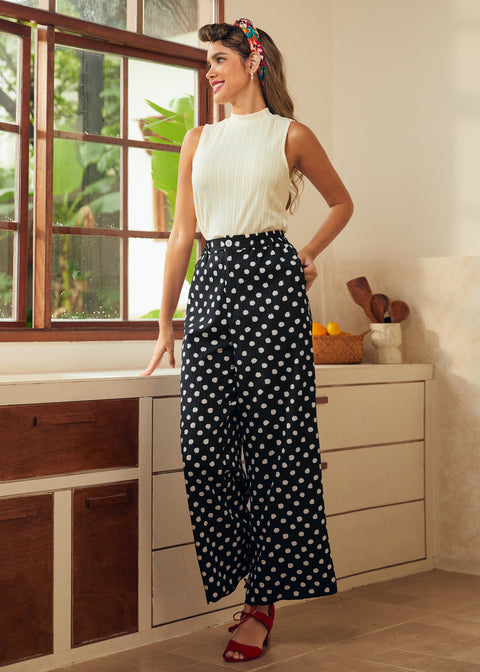 Woman in a white sleeveless top and black polka dot pants standing in a kitchen.