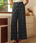 Lady wearing black polka dot pants with a white top in a kitchen setting.