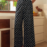Lady wearing black polka dot pants with a white top in a kitchen setting.