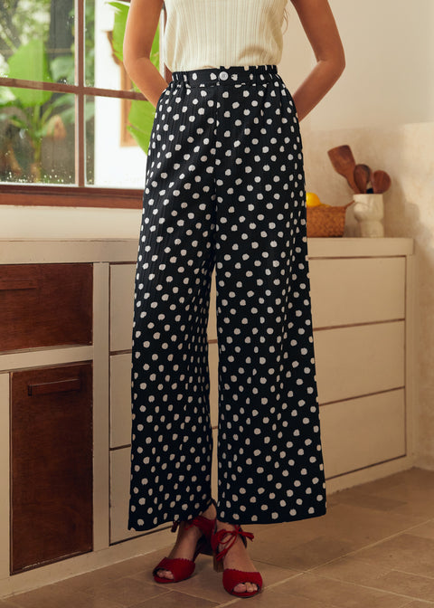 Lady wearing black polka dot pants with a white top in a kitchen setting.