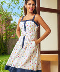 Woman wearing a belted white dress with colorful nautical patterns, standing outdoors.