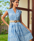 Woman wearing a blue vintage style summer dress with a tan belt standing outdoors.