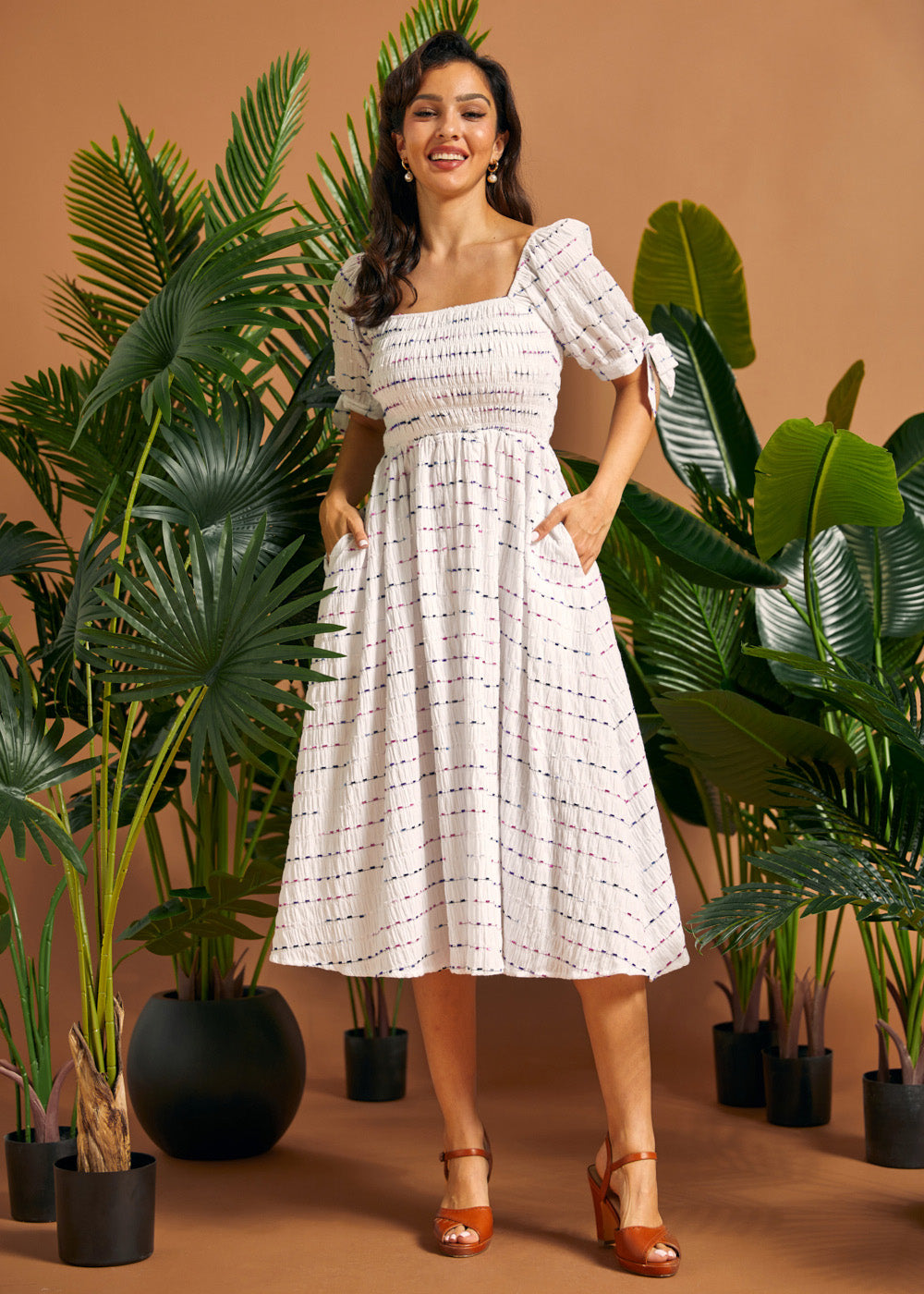 Woman wearing a white smocked square neck midi dress with colorful textured stripes, puff sleeves, and pockets.