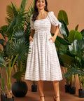 Woman wearing a white smocked square neck midi dress with colorful textured stripes, puff sleeves, and pockets.
