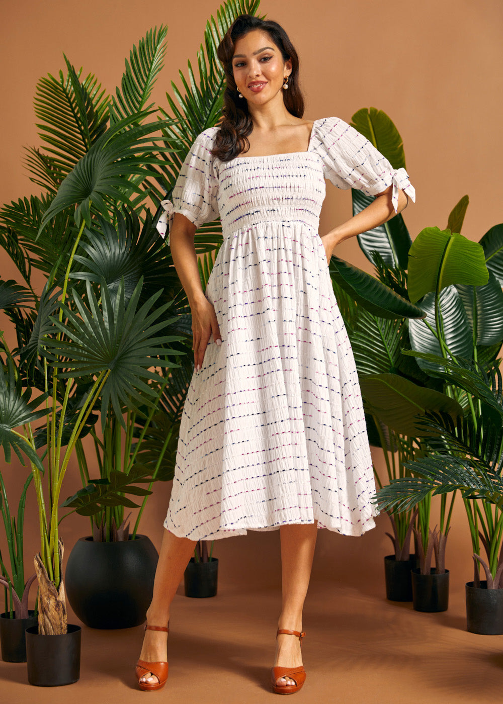 Full-length view of a woman wearing a white square neck midi dress with smocking, tie sleeves, and colorful stitched stripes.