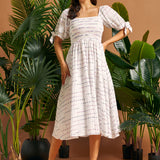 Full-length view of a woman wearing a white square neck midi dress with smocking, tie sleeves, and colorful stitched stripes.