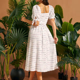 Back view of a woman wearing a white smocked midi dress with a square back neckline and tie sleeve details.