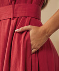 Close-up of a woman wearing a dusty red midi dress with a matching waist belt and a side pockets.