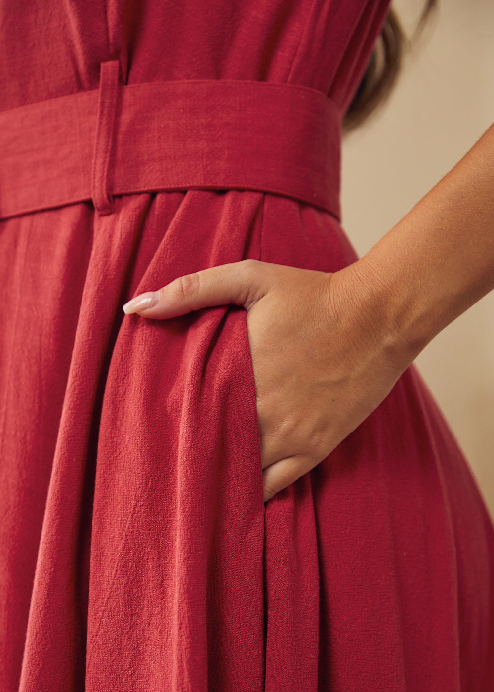 Close-up of a woman wearing a dusty red midi dress with a matching waist belt and a side pockets.
