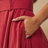 Close-up of a woman wearing a dusty red midi dress with a matching waist belt and a side pockets.