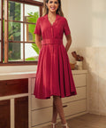 A woman modeling a short-sleeve, collared, belted A-line dress in a vintage red color.