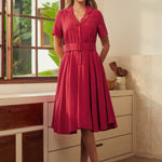 A woman modeling a short-sleeve, collared, belted A-line dress in a vintage red color.