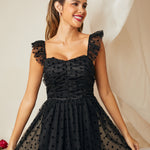 Woman wearing a black polka dot dress with sheer sleeves against a neutral background