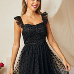 Woman wearing a black polka dot dress with sheer sleeves against a neutral background