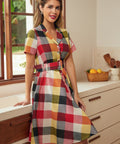 Woman wearing a colorful wine, mustard, pink, and charcoal plaid dress with short sleeves.