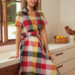 Woman wearing a colorful wine, mustard, pink, and charcoal plaid dress with short sleeves.