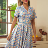 Woman wearing a vintage-inspired blue plaid dress with cherry print and short sleeves.