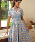 Woman wearing a retro cotton dress featuring tiny cherry motifs and a notched collar.