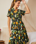 Woman wearing a black cotton shirt dress with oranges, lemons, blossoms, and leafy botanical print.