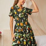 Woman wearing a black cotton shirt dress with oranges, lemons, blossoms, and leafy botanical print.