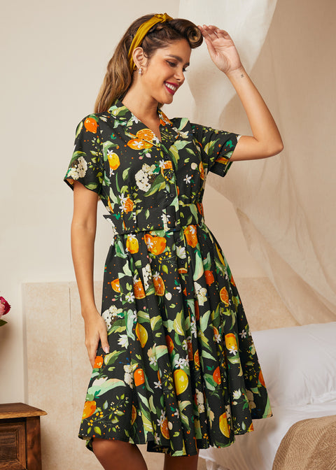 Woman wearing a black cotton shirt dress with oranges, lemons, blossoms, and leafy botanical print.