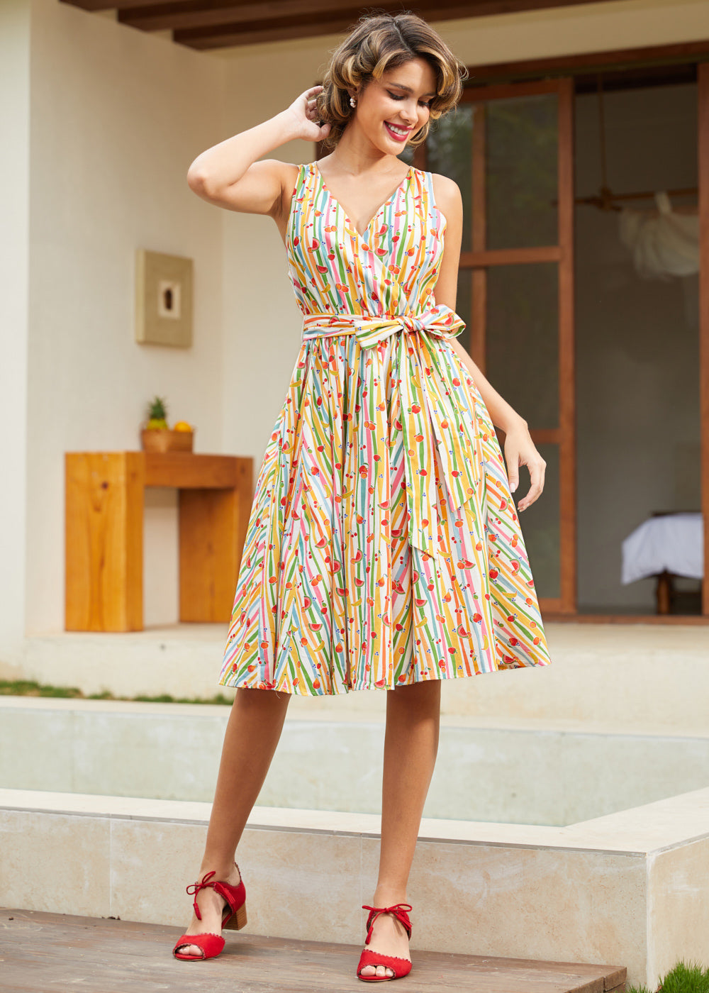 Woman wearing a sleeveless fit-and-flare dress featuring a playful fruit stripe novelty print.