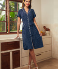 Woman wearing a vintage-inspired navy polka dot shirt dress with contrast piping, tie waist, and short sleeves.