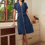 Woman wearing a vintage-inspired navy polka dot shirt dress with contrast piping, tie waist, and short sleeves.