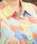 Close-up of a sleeveless collared button-front shirt dress with an allover patchwork umbrella print in yellow, blue, red, green, and white.