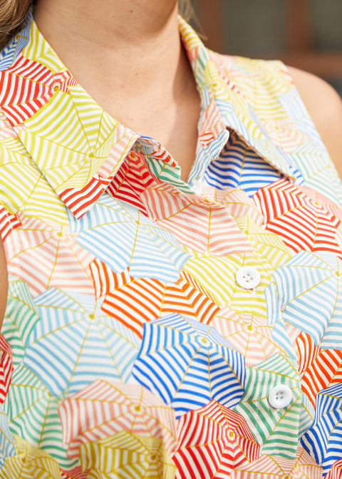 Close-up of a sleeveless collared button-front shirt dress with an allover patchwork umbrella print in yellow, blue, red, green, and white.