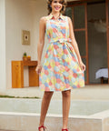 A woman models a sleeveless, collared A-line dress with a colorful geometric pattern in shades of yellow, pink, blue, and green.