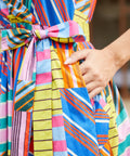 Close-up of a woman wearing a brightly striped and patchwork-patterned dress with a matching tie belt, and pockets.