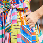 Close-up of a woman wearing a brightly striped and patchwork-patterned dress with a matching tie belt, and pockets.