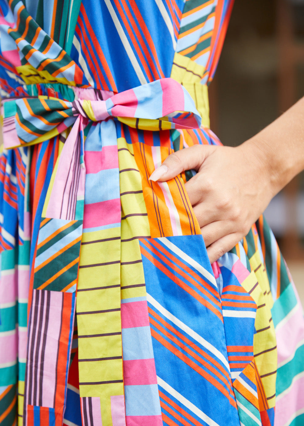 Close-up of a woman wearing a brightly striped and patchwork-patterned dress with a matching tie belt, and pockets.