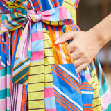 Close-up of a woman wearing a brightly striped and patchwork-patterned dress with a matching tie belt, and pockets.