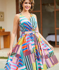 A woman modeling a sleeveless wrap-style A-line dress with a vibrant multicolor geometric stripe and patchwork print.