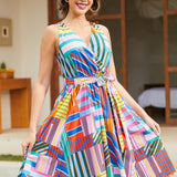 A woman modeling a sleeveless wrap-style A-line dress with a vibrant multicolor geometric stripe and patchwork print.